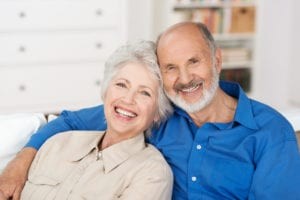 Older Couple Smiling Sitting On Couch At Home